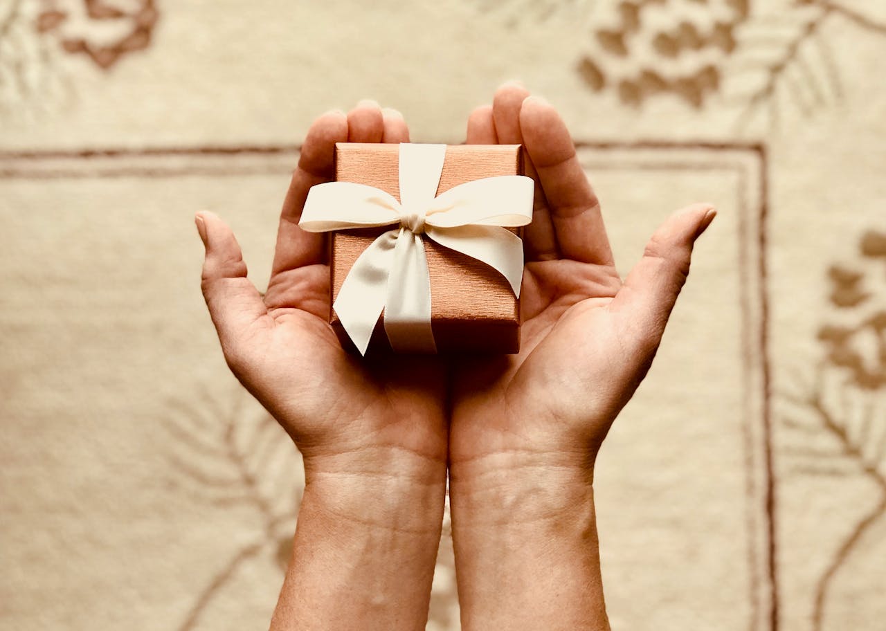 Home Close-up of hands holding a beautifully wrapped gift box with a ribbon, perfect for celebrations and surprises.